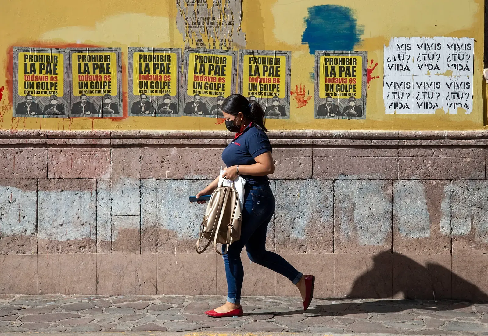 Mujer caminando frente a un muro con carteles de la campaña por la PAE.